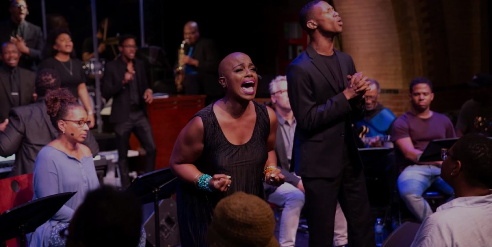 Theater Of War Hero Image of a Woman Performing on Stage in front of a Choir